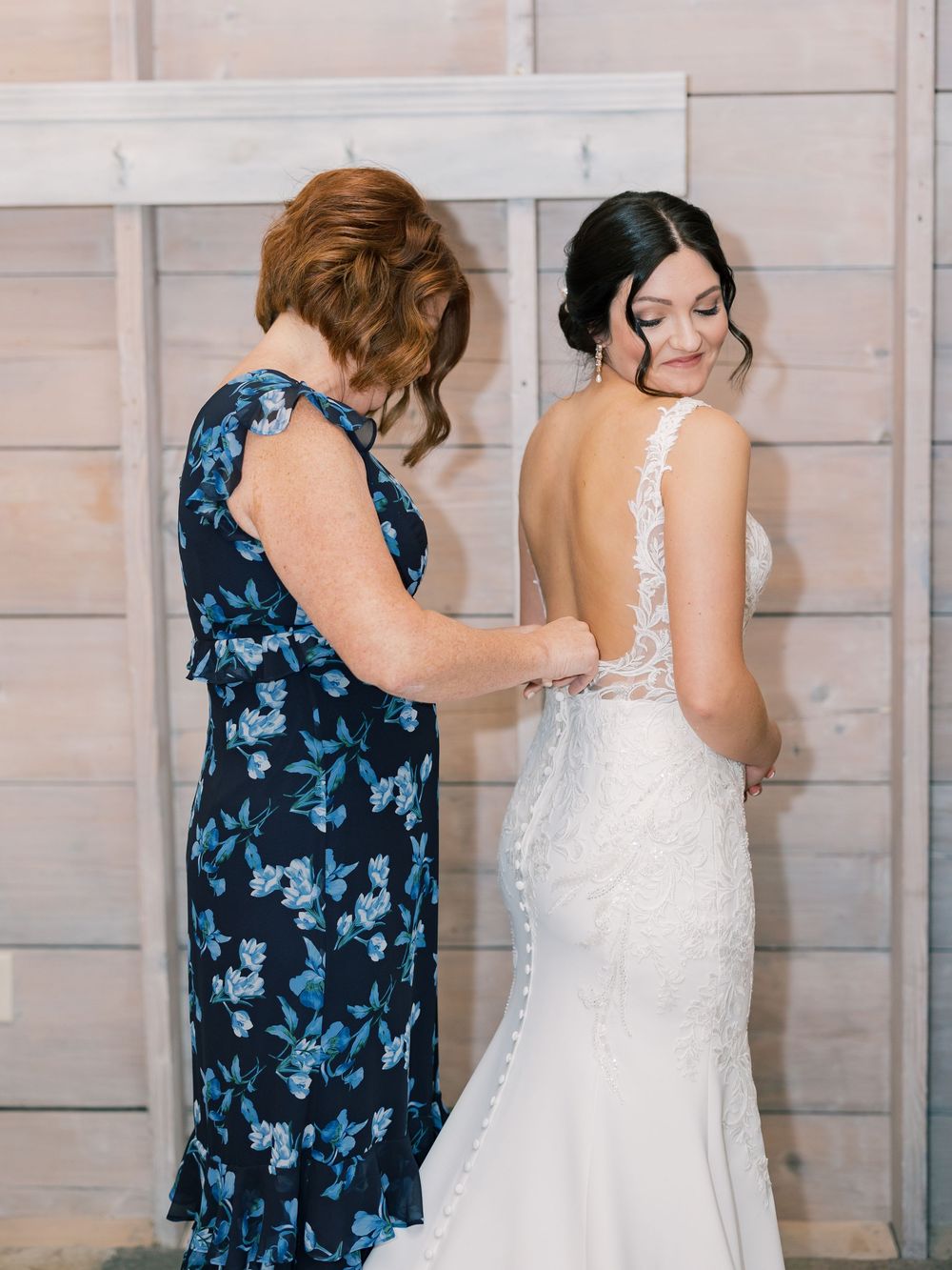A touching pre-wedding moment as someone helps adjust a beautiful white lace wedding gown.
