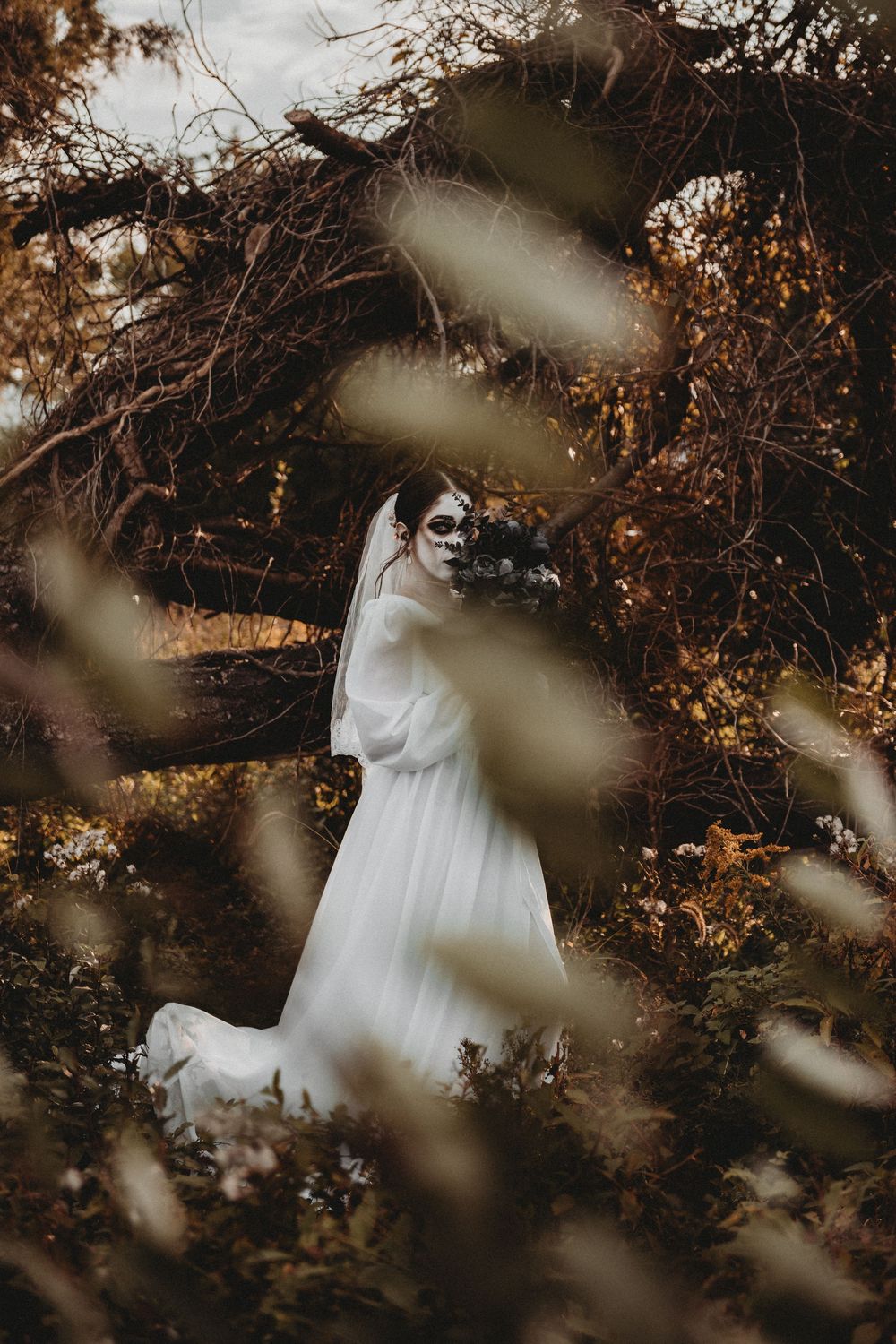 A figure in a flowing white dress stands among autumn trees and branches creating a dreamy ethereal scene.