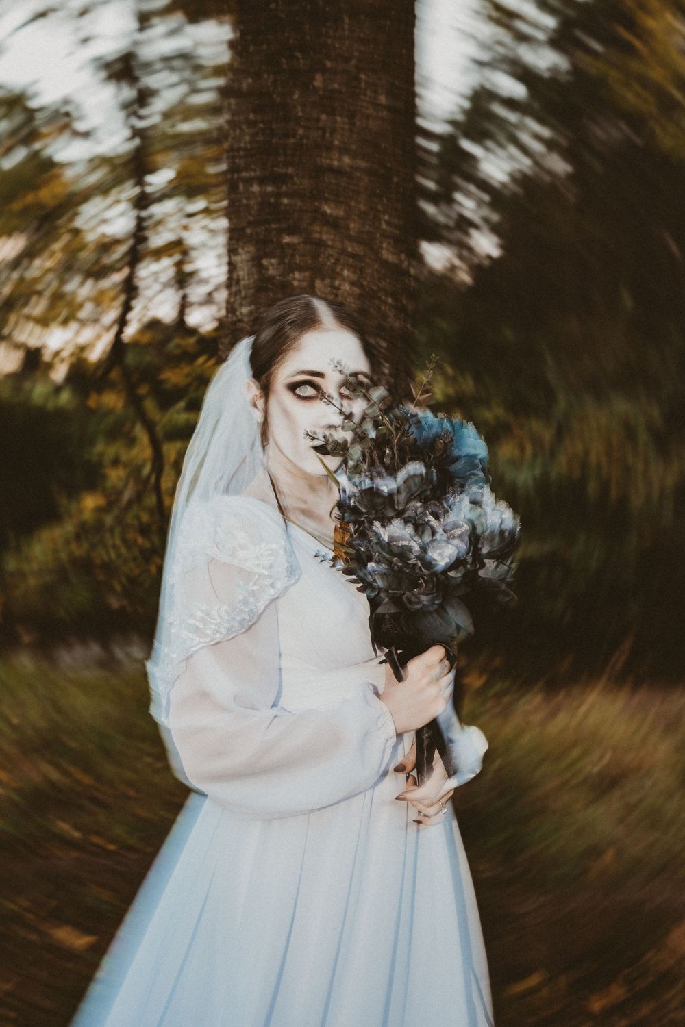 Elegant bride in white wedding dress exhaling wisps of smoke surrounded by blurred autumn trees in a cinematic scene.