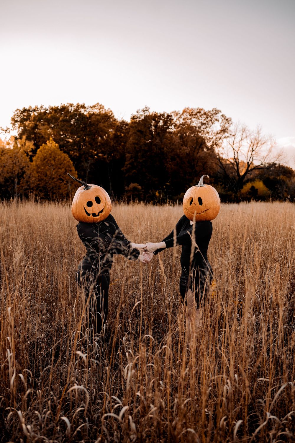 Two figures wearing pumpkin masks stand in a golden autumn field on a moody overcast day.