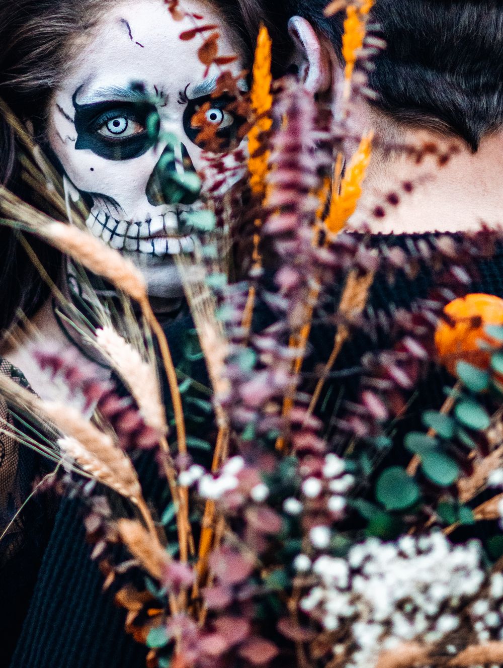 Creative Day of the Dead makeup with colorful feathers and intricate skull face paint design captured in artistic portrait.
