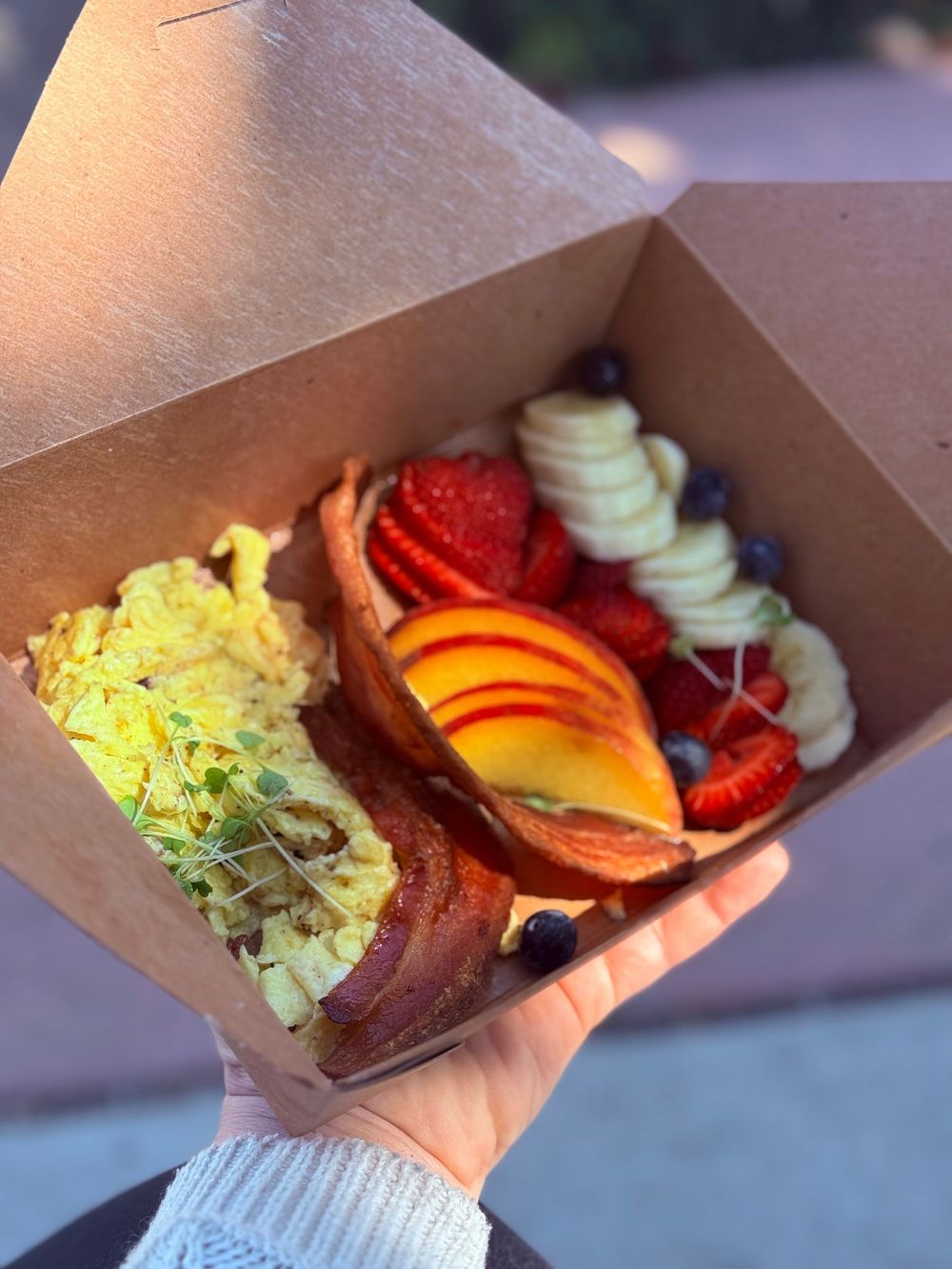 Fresh fruit bowl filled with colorful strawberries, oranges, and bananas served in a takeout container.