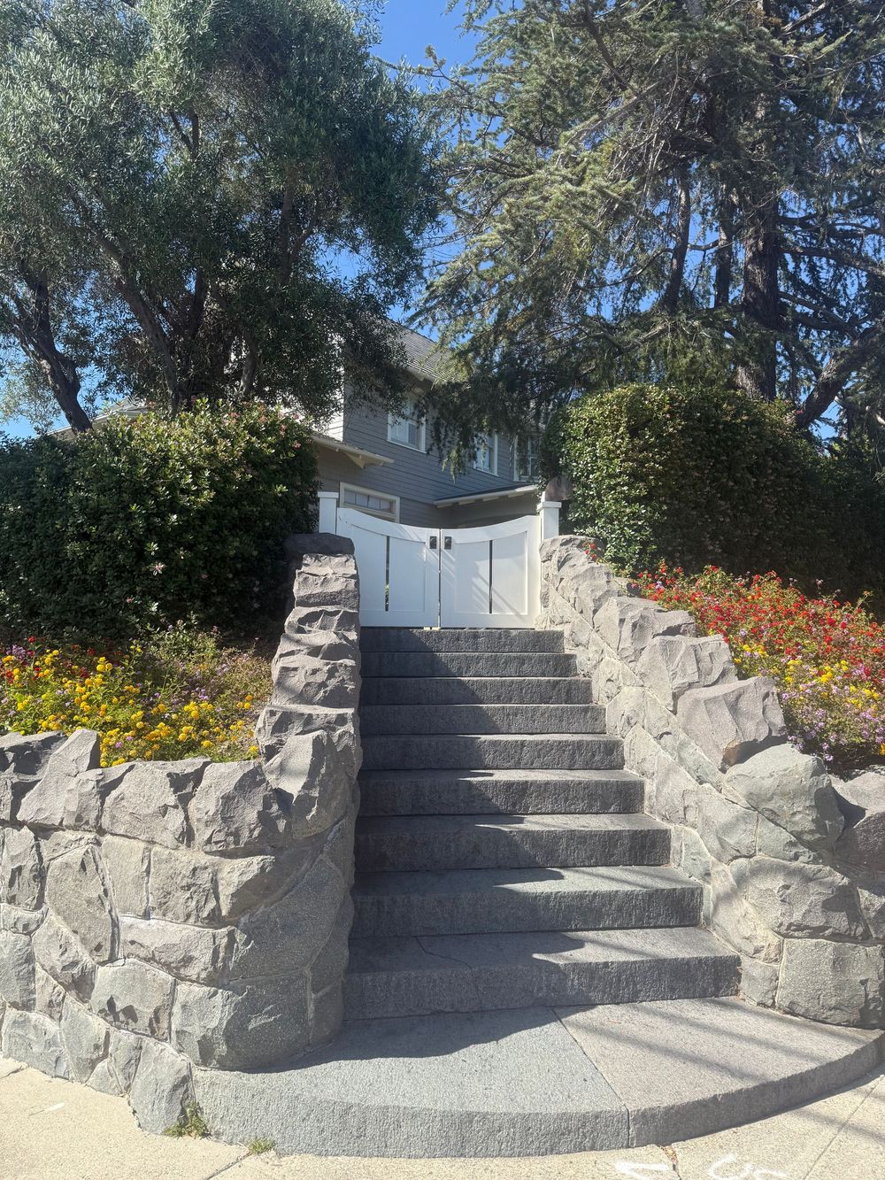 Stone stairway with curved walls and colorful flowers leads up to a white building through a serene garden setting.
