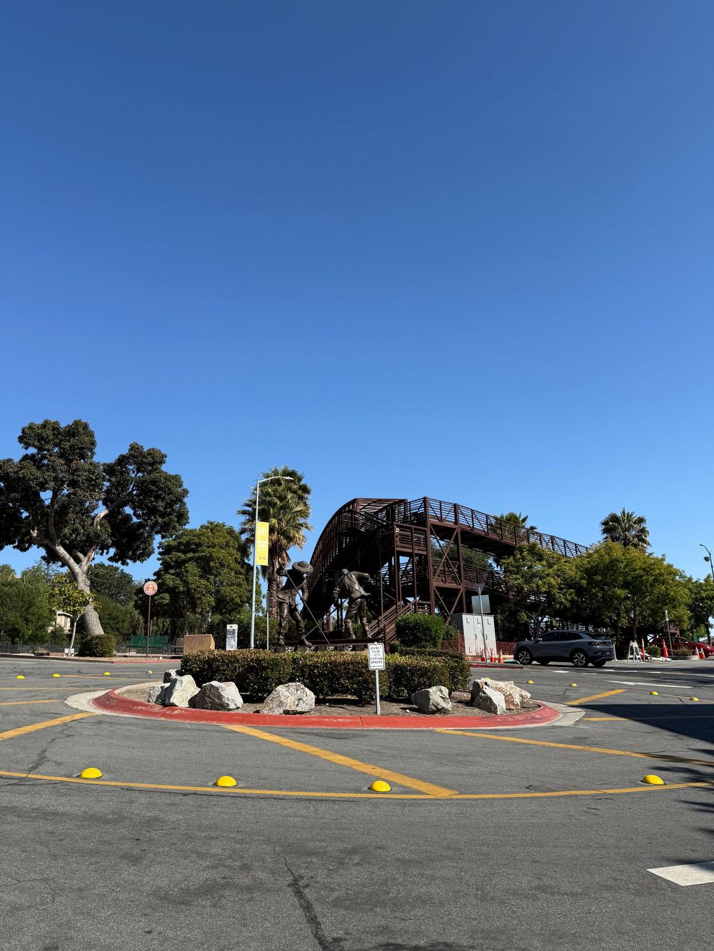 Three views of an empty parking lot median with decorative rocks and trees under a bright blue sky.