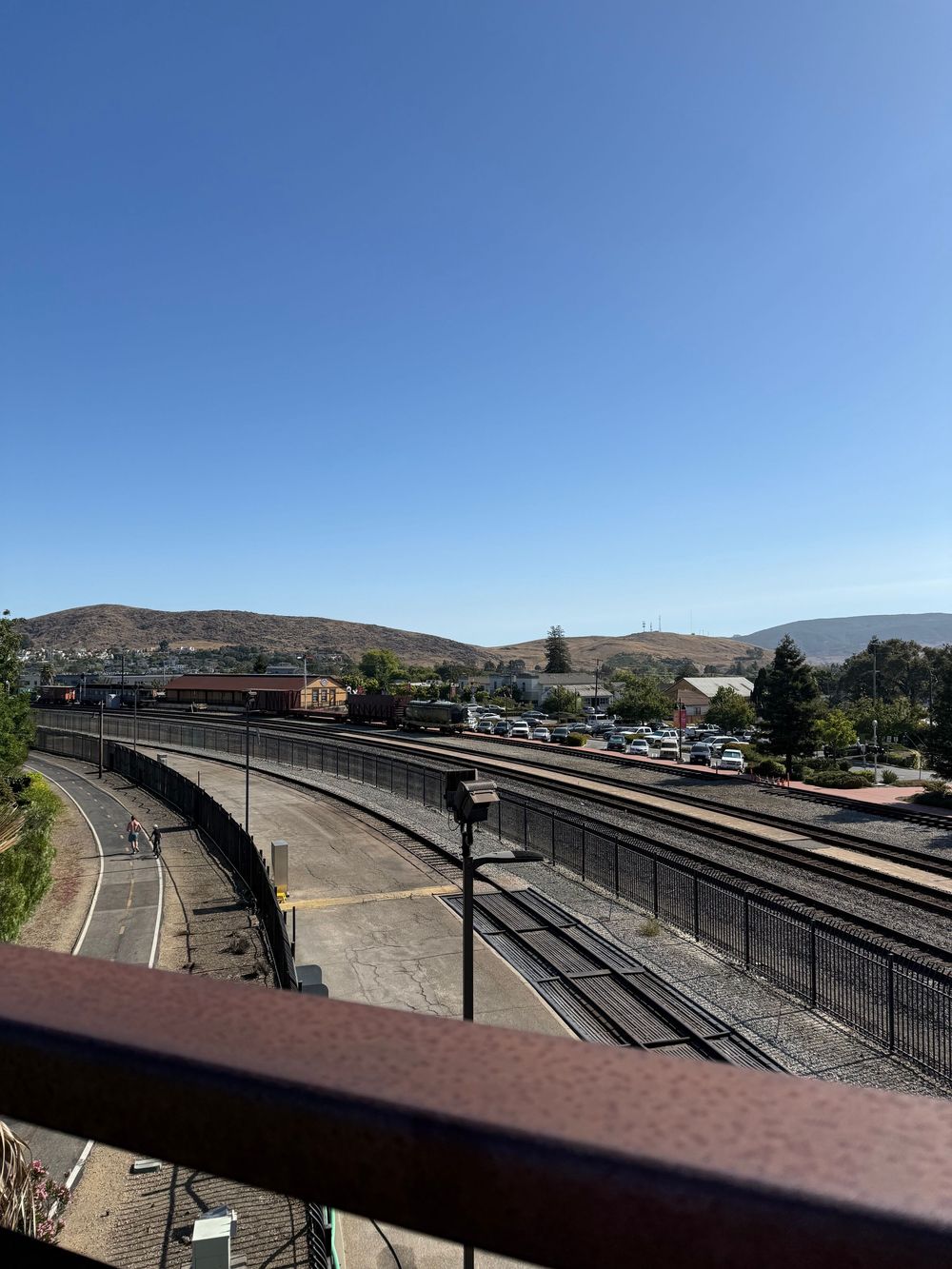 Panoramic view of multiple train tracks and platforms at a railway station with mountains visible in the background.