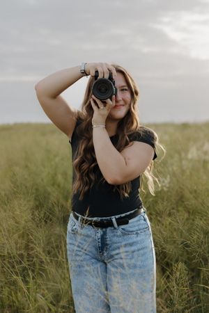 A photographer practices different poses while holding a camera in a grassy field.