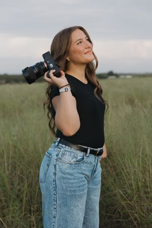 A photographer in casual attire takes photos in a natural grassland setting.