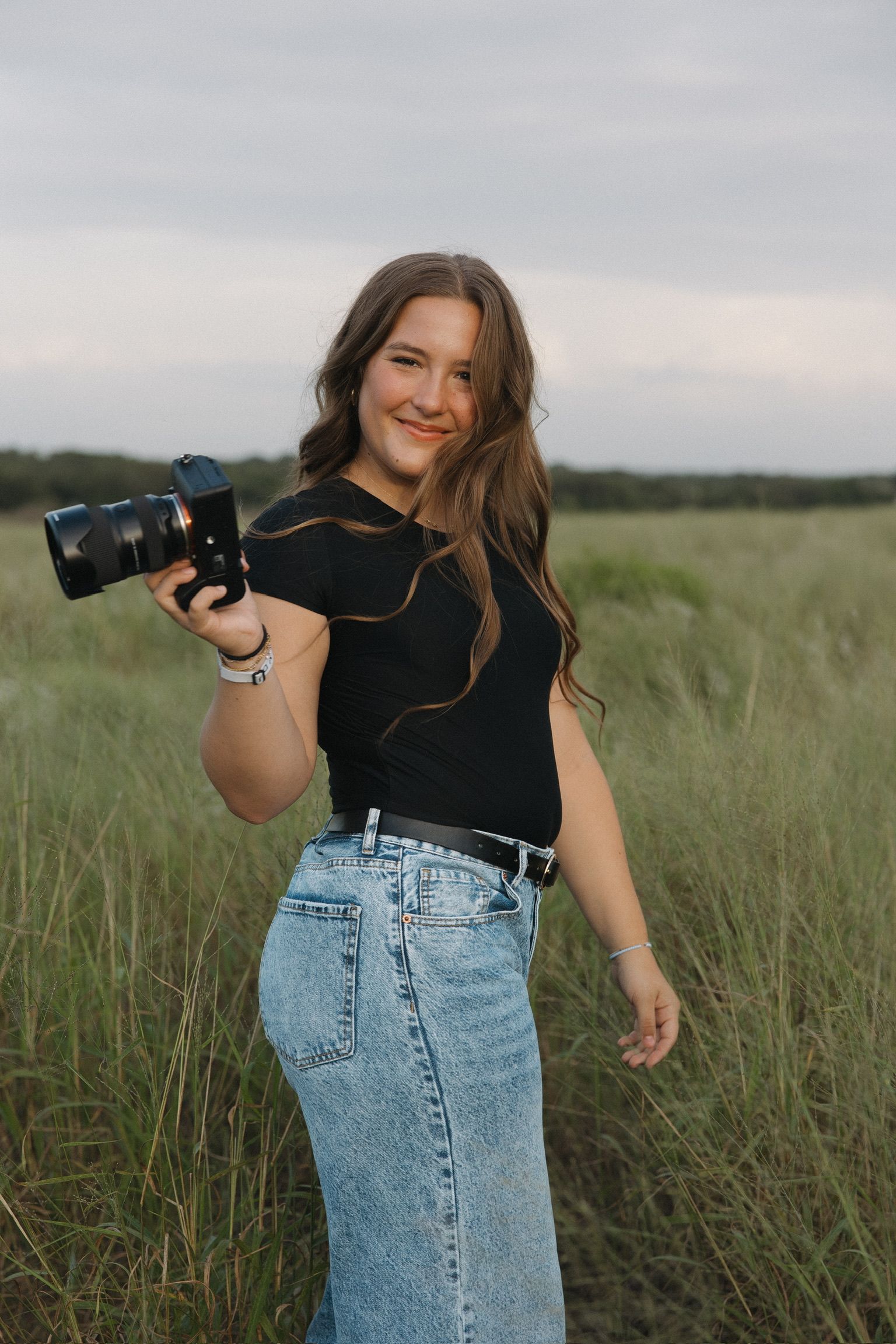 A photographer demonstrates dynamic poses with camera equipment in an outdoor field.