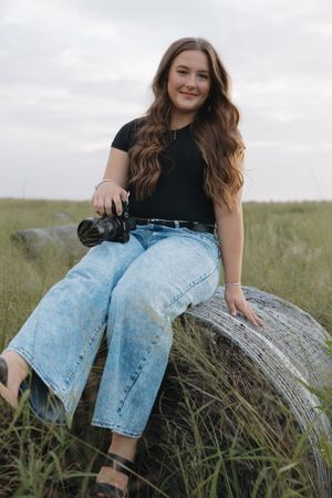 A photographer relaxes on a fallen log surrounded by tall grass in a natural setting.