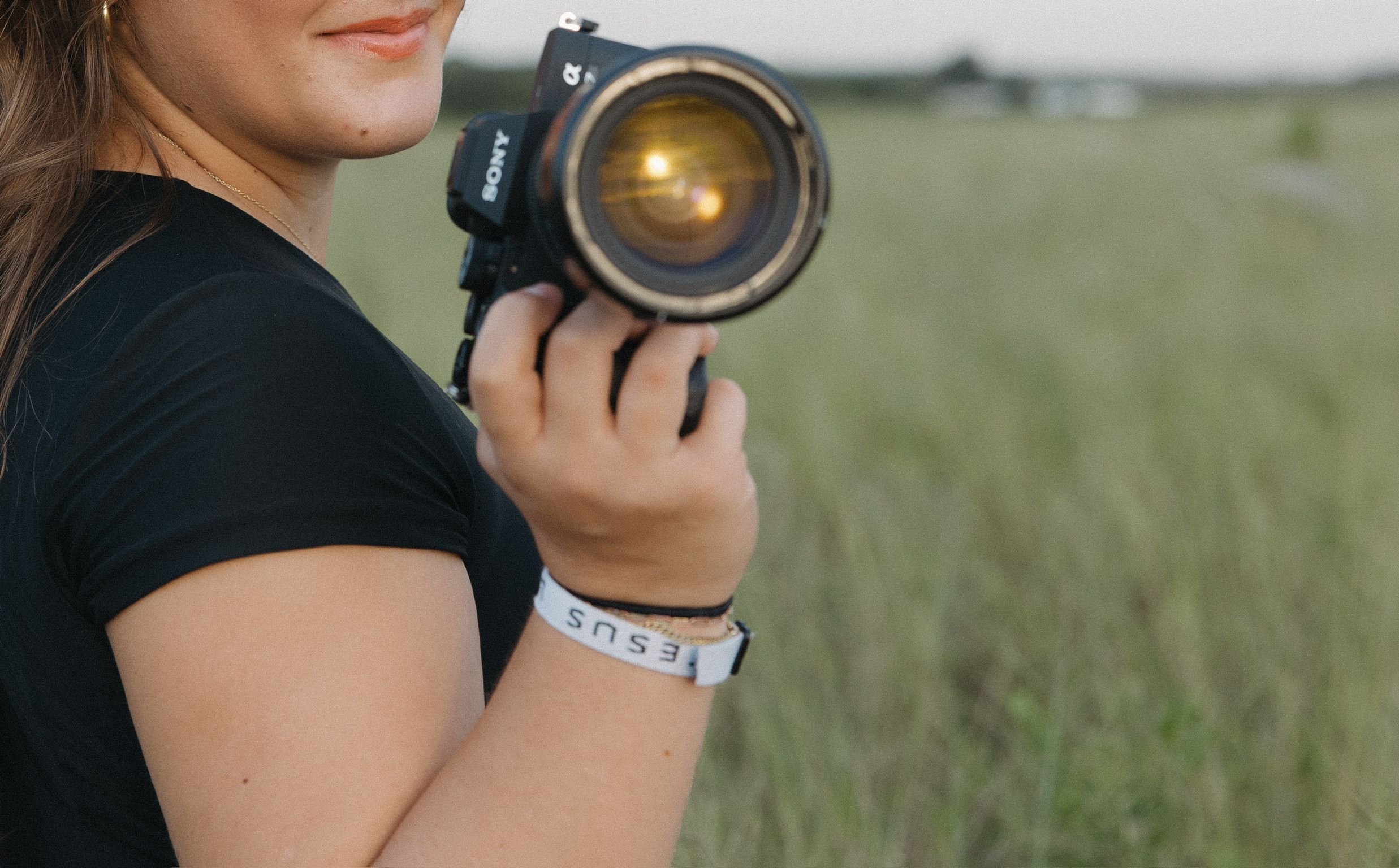 Close-up of photographer holding professional camera with watch in grassy field.