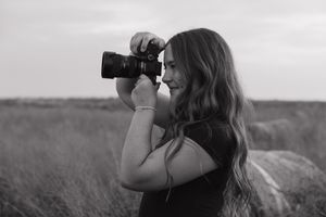 Black and white photo of photographer with camera in outdoor field setting.