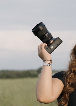 Professional camera with telephoto lens held up against cloudy sky in outdoor setting.