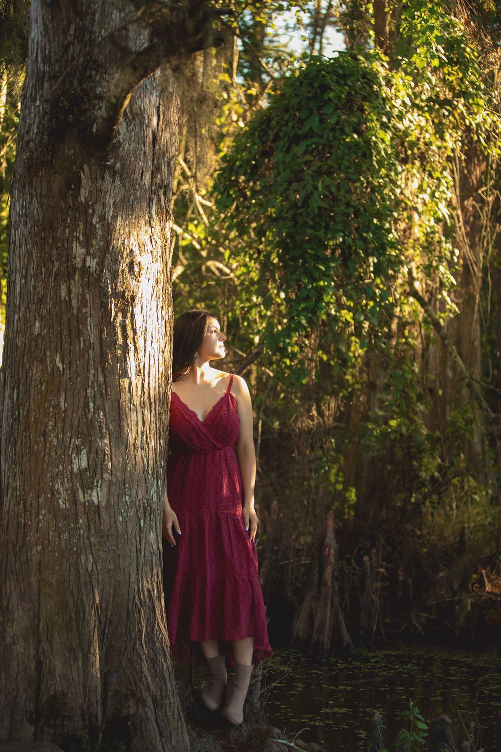 A romantic scene in a forest with a burgundy dress and dramatic lighting among old cypress trees and Spanish moss.