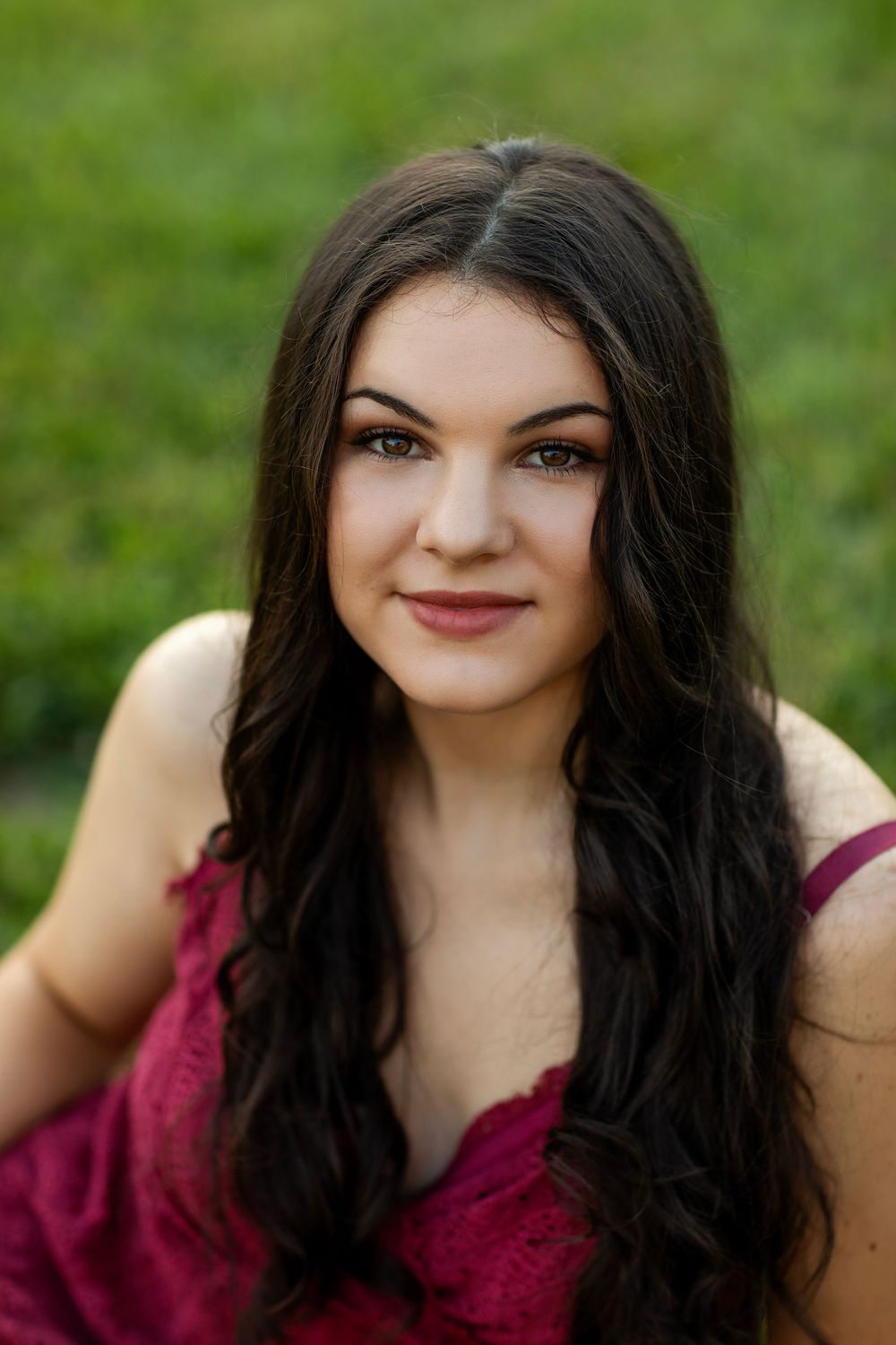 Close up portrait series against a green background wearing a burgundy top with dark flowing hair.