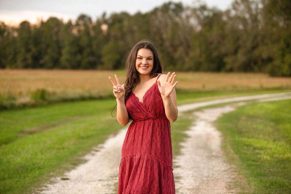 Woman in flowing red dress stands in golden field during sunset along dirt path creating dreamy outdoor portrait.