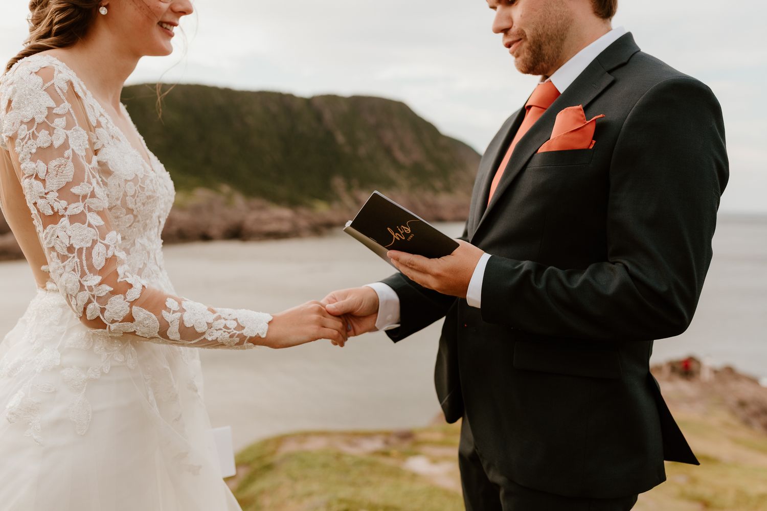 bride and groom reading their vows on a Newfoundland cliff while holding hands