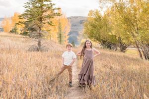 Family walking together through golden autumn fields with tall grass and evergreen trees at sunset.