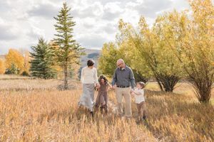A family walks through a golden autumn field with tall grass and evergreen trees at sunset.