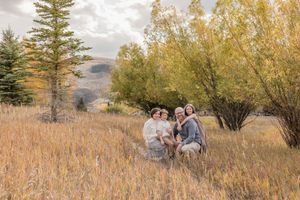 A couple and their horse stand together in a golden autumn field with evergreen trees in the background.