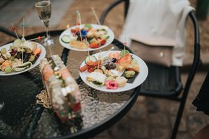 Elegant appetizers and hors d'oeuvres displayed on plates with wine glasses on a reflective dark table surface.