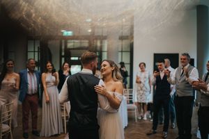 A couple shares their first dance on a wedding reception dance floor while guests look on in the background.