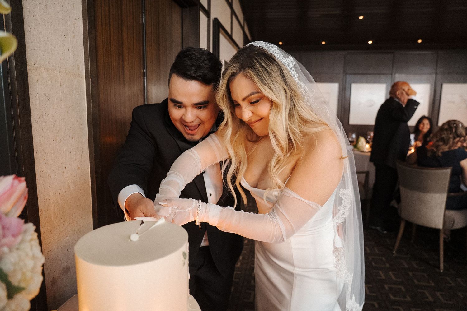 A bride and groom share a joyful moment together while cutting their wedding cake at an intimate reception.