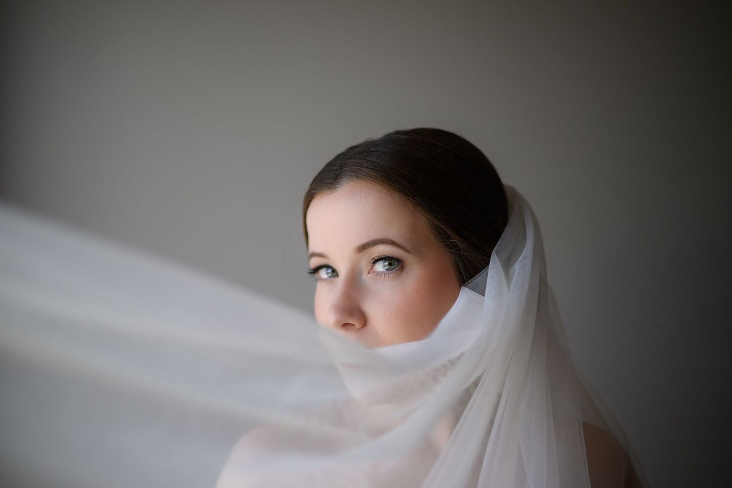 Dreamy bridal portrait with flowing white veil in soft window light.