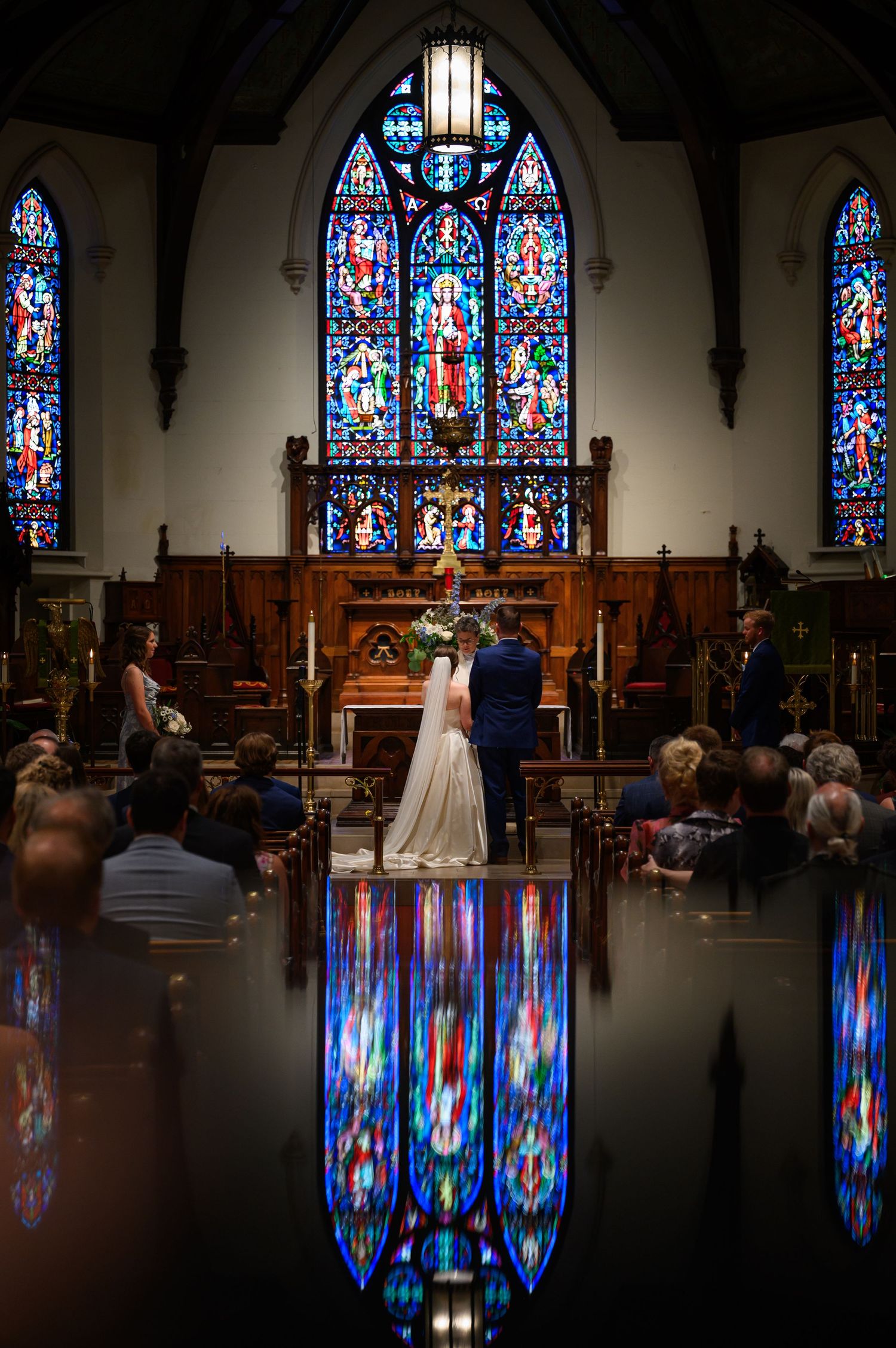 A wedding ceremony in a church with stunning stained glass windows creating colorful reflections on the floor.
