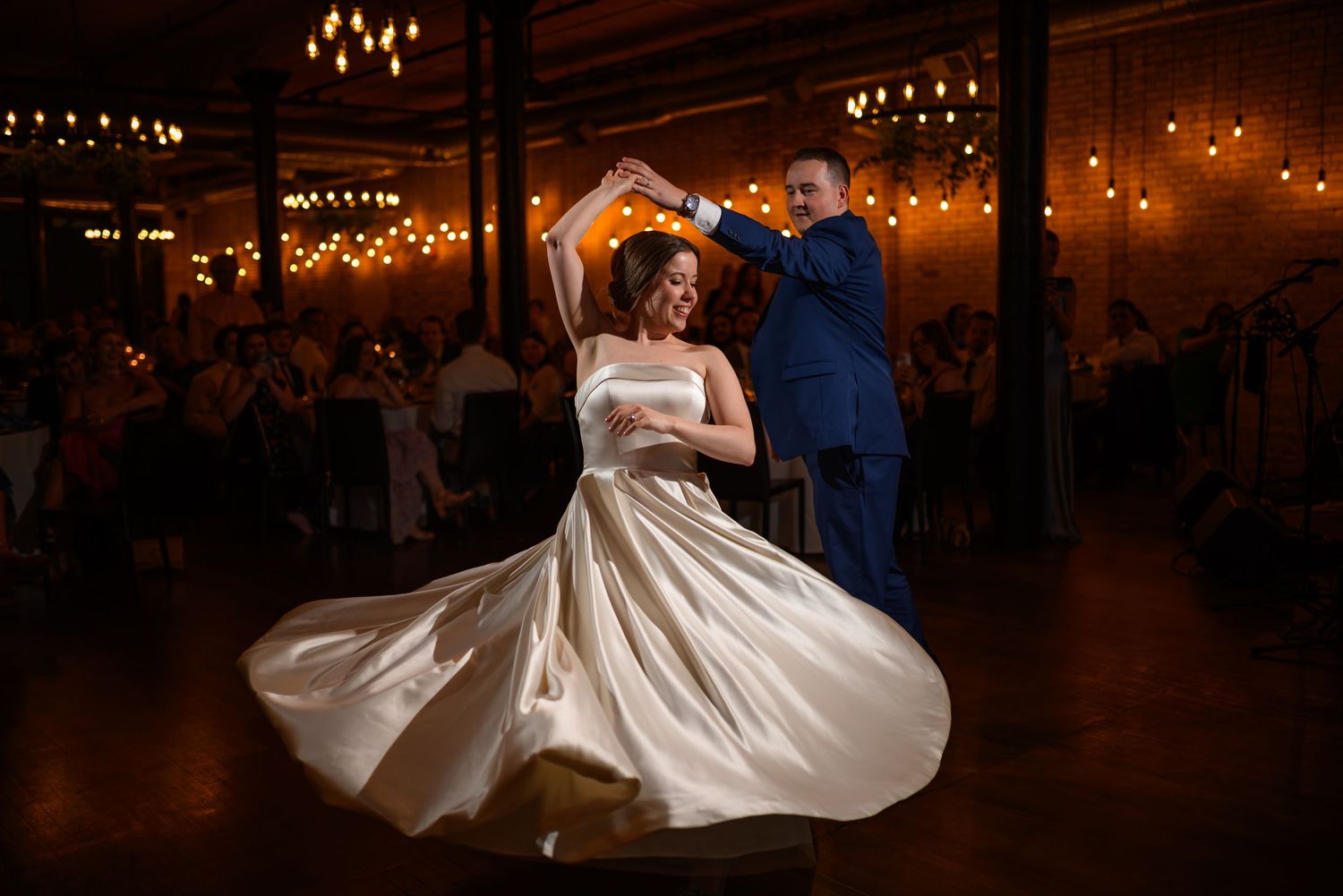 Dancing couple twirling on dance floor under warm reception lighting.