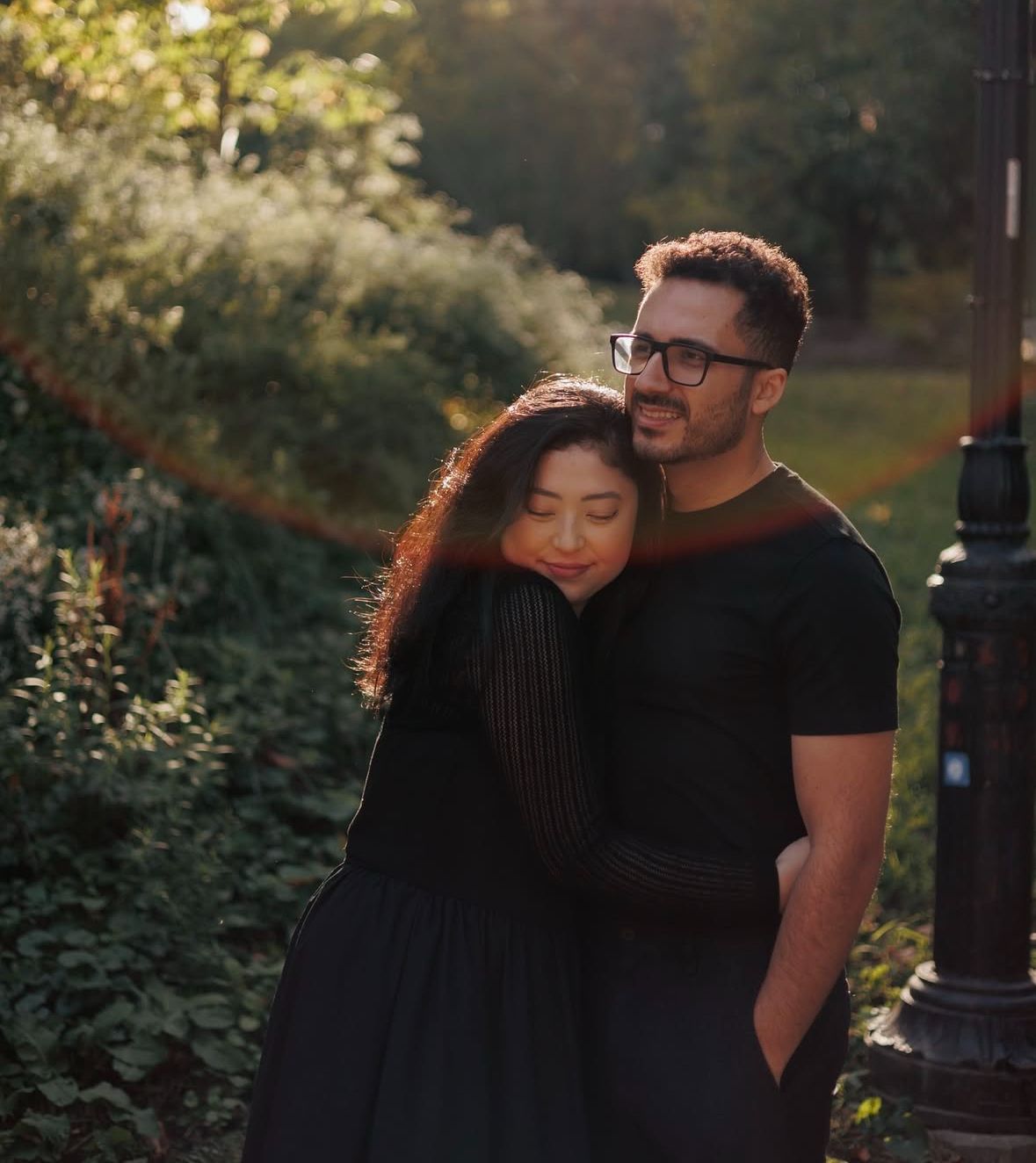 Intimate embrace between couple during golden hour in urban garden setting.