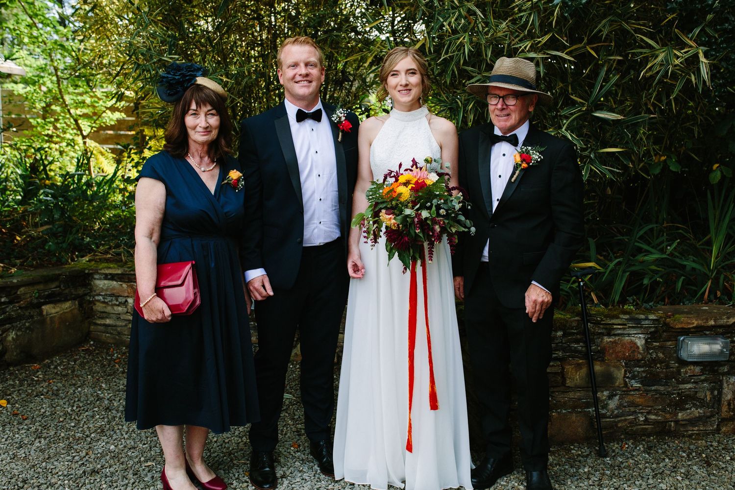 Wedding party stands together outdoors with greenery and stone pathway in the background.