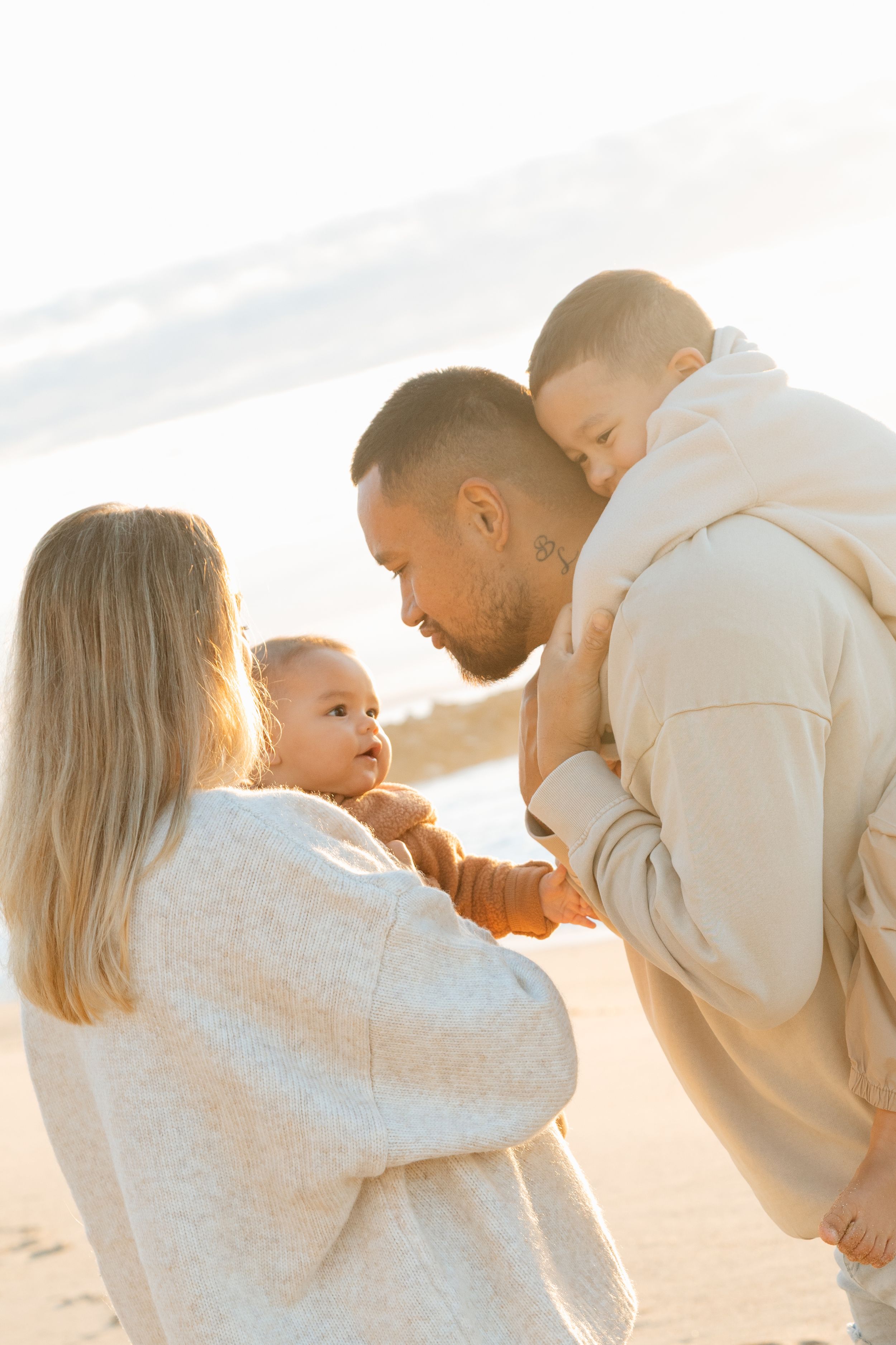 Three warm sunlit images show tender family moments at the beach in white outfits during golden hour.