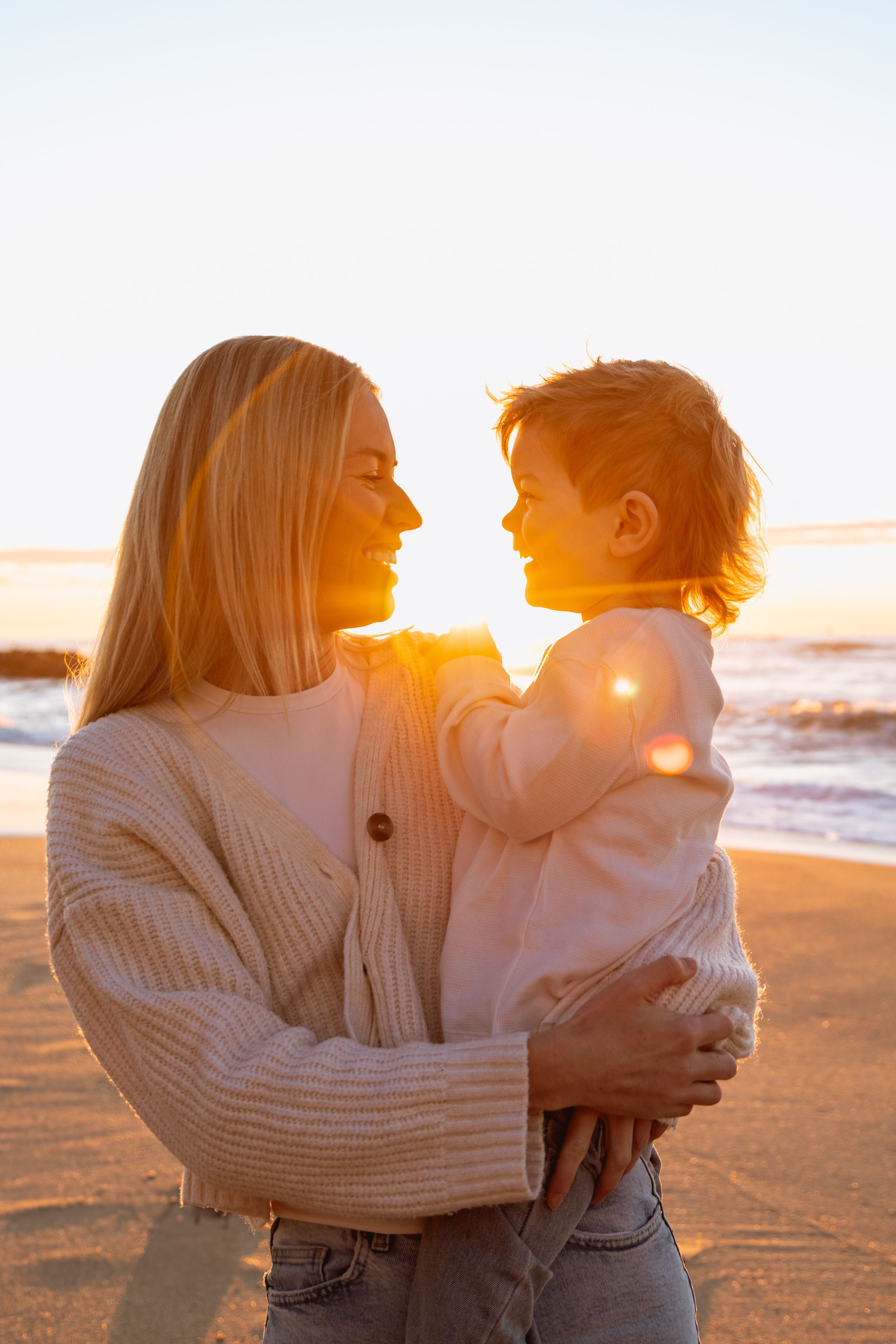 Family embraces on sunny beach at sunset while waves crash behind them on the golden sand.