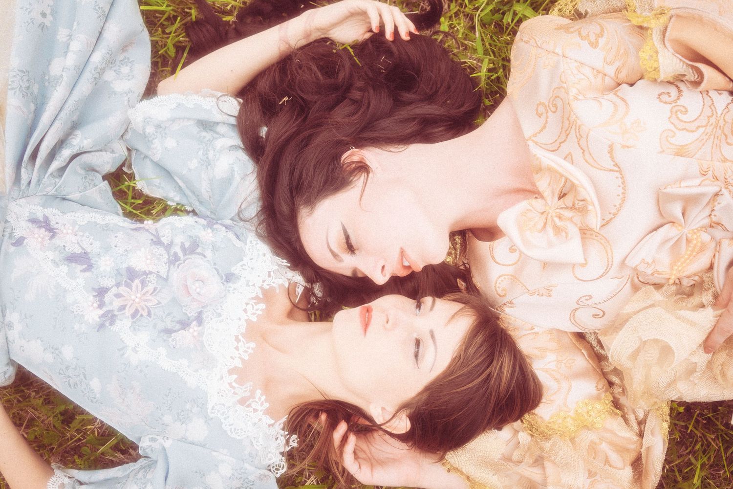 A woman in a pink lace dress lies peacefully on grass with flowers in an ethereal spring setting.