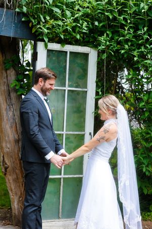 A couple shares a tender moment on their wedding day in front of a vintage door surrounded by green foliage.