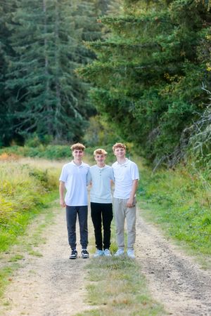 Three young individuals in light-colored clothing walking together on a dirt path through a wooded area.