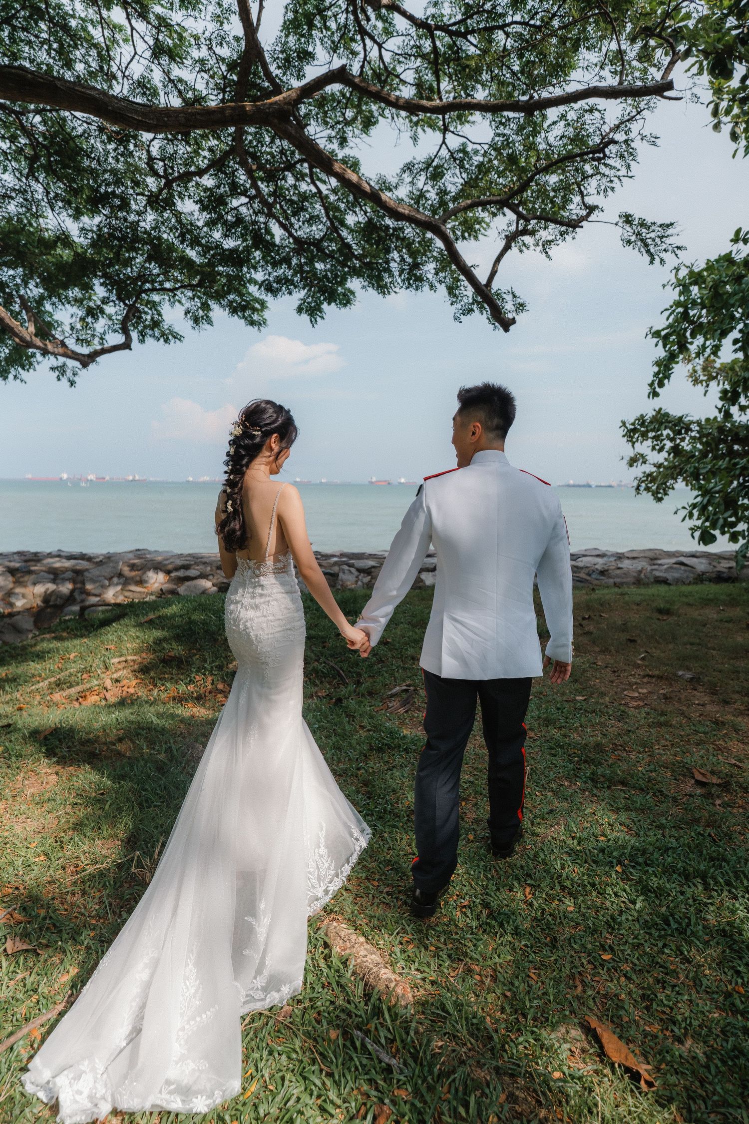 A romantic wedding couple holds hands while overlooking the ocean from a scenic cliffside location.