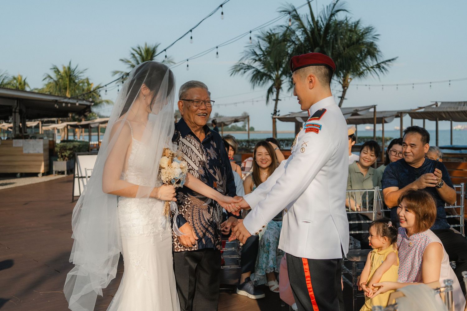 Outdoor beach wedding reception gathering at sunset with guests enjoying the waterfront atmosphere.