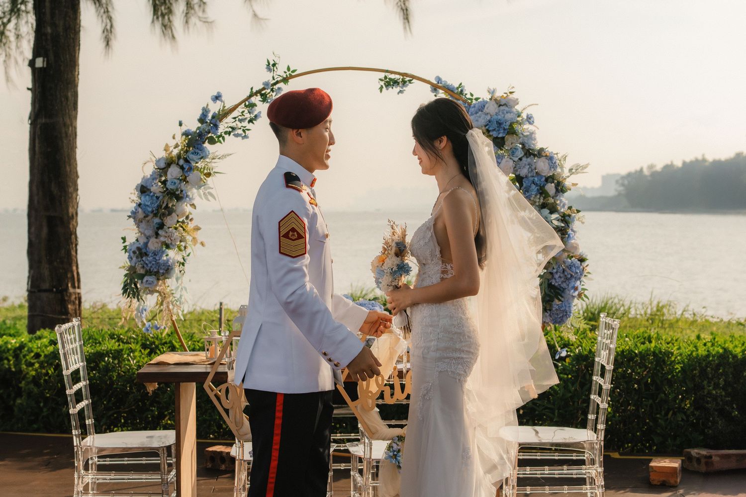 Wedding ceremony setup with floral arch overlooking waterfront during sunset.