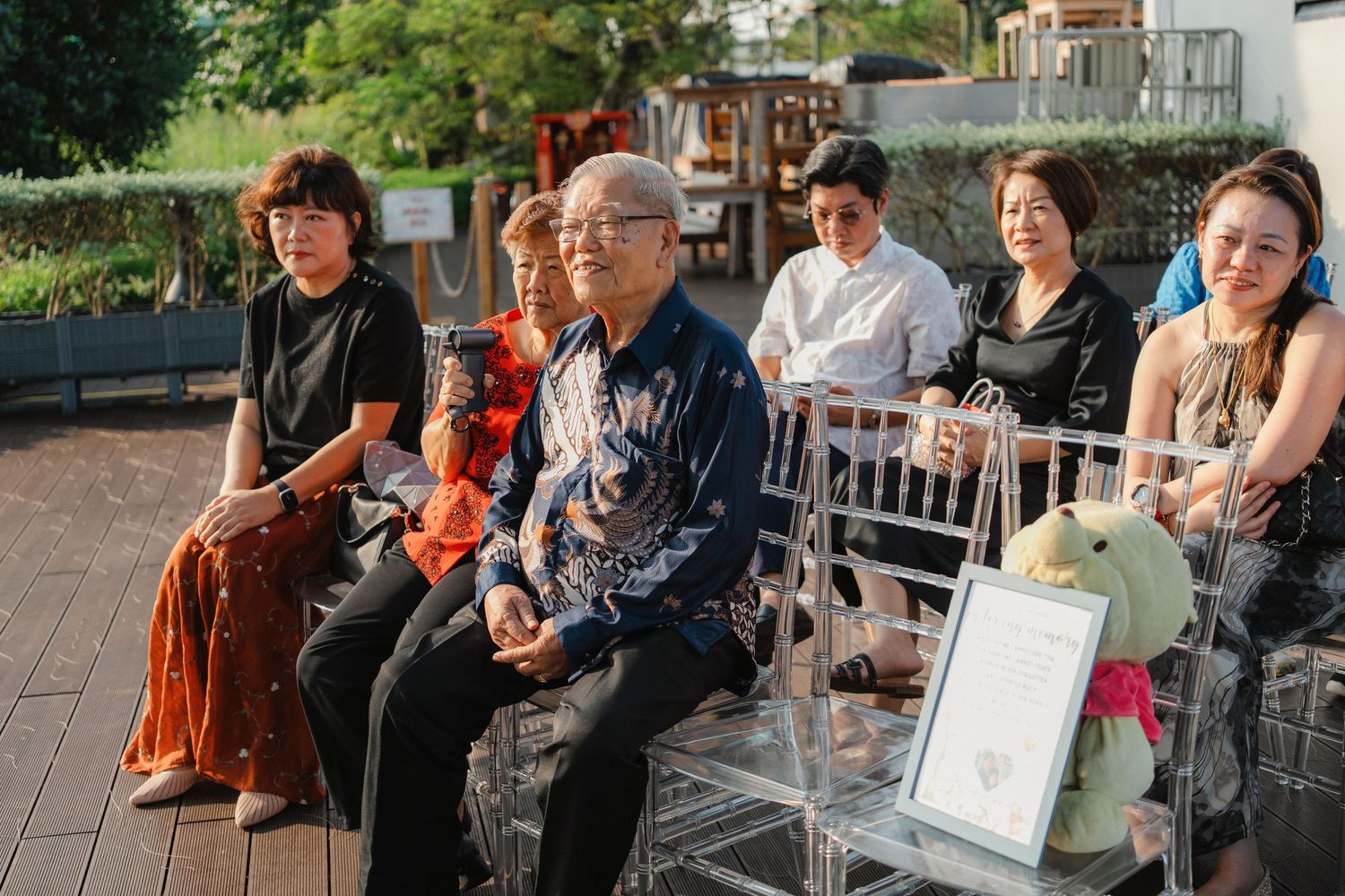 Wedding guests seated on white chairs during outdoor ceremony.