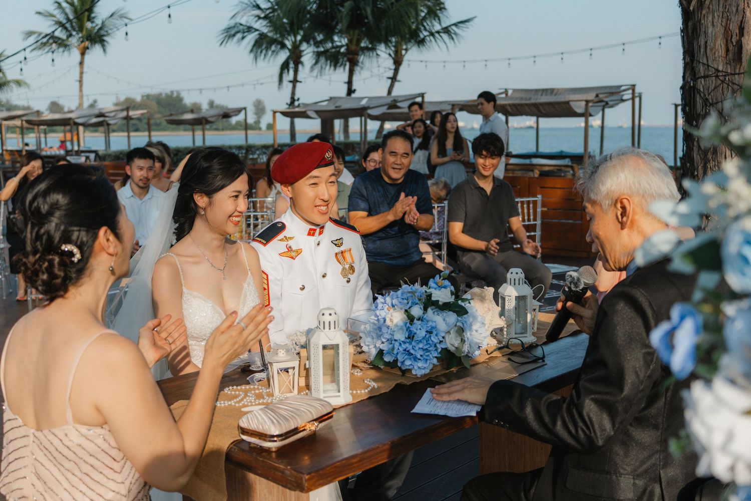 Wedding reception gathering with blue floral centerpieces and palm trees in background.