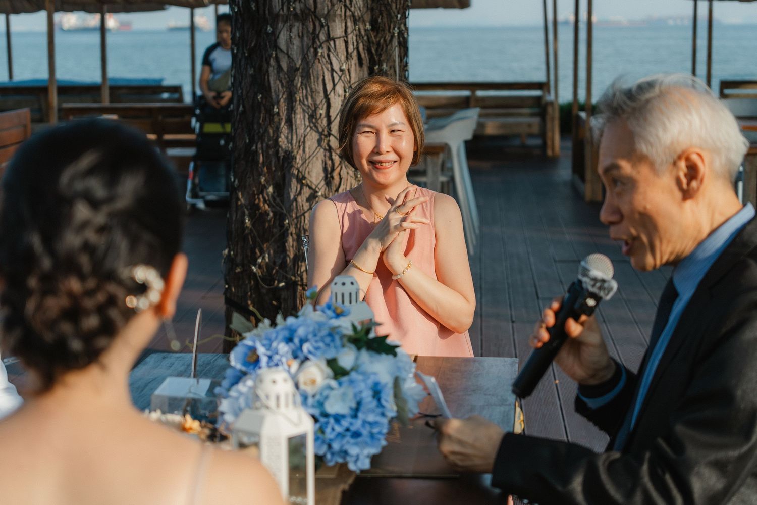 Wedding celebration group shares joyful moments on a waterfront venue with blue skies in background.