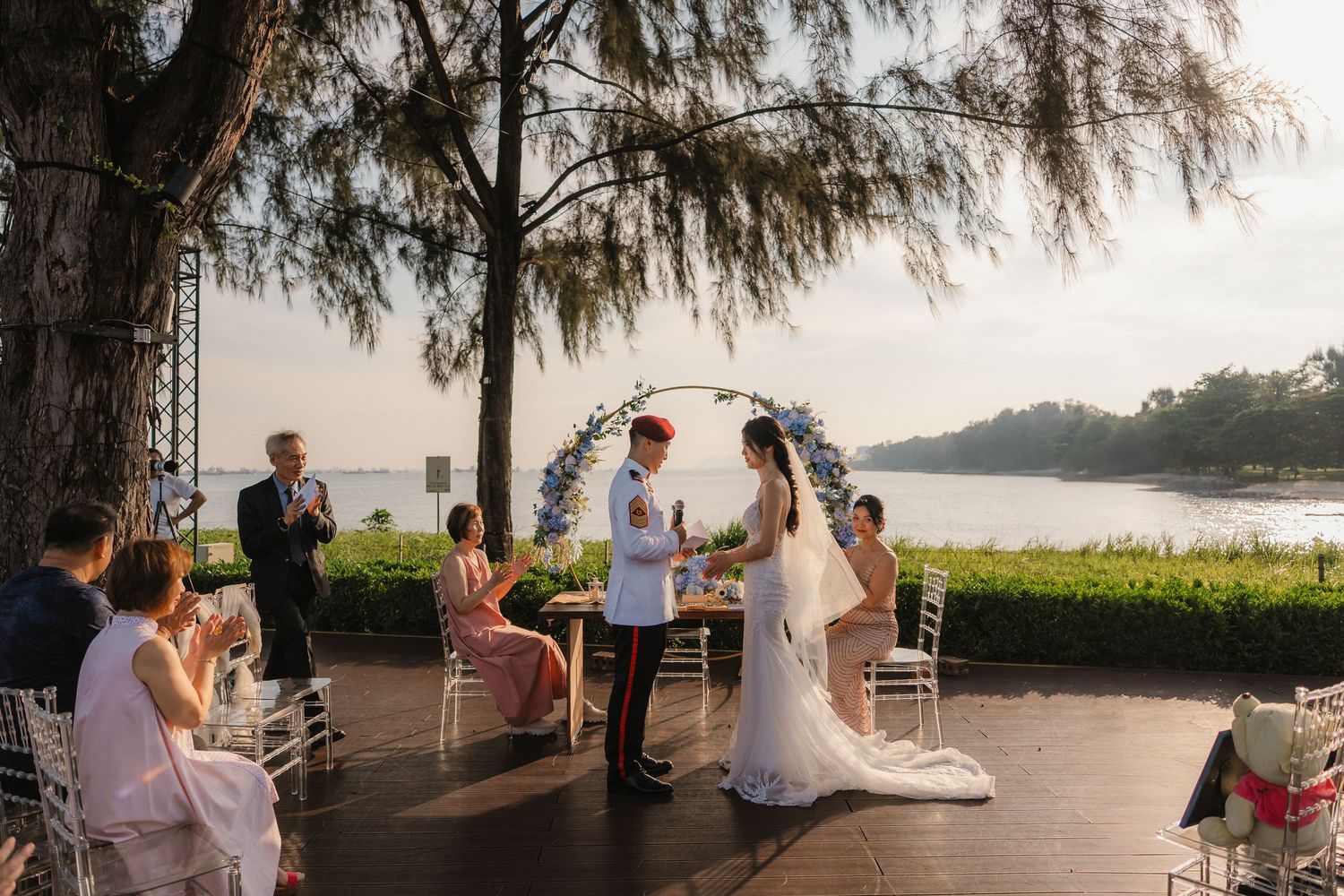Wedding celebration on waterfront deck with palm trees and ocean view.