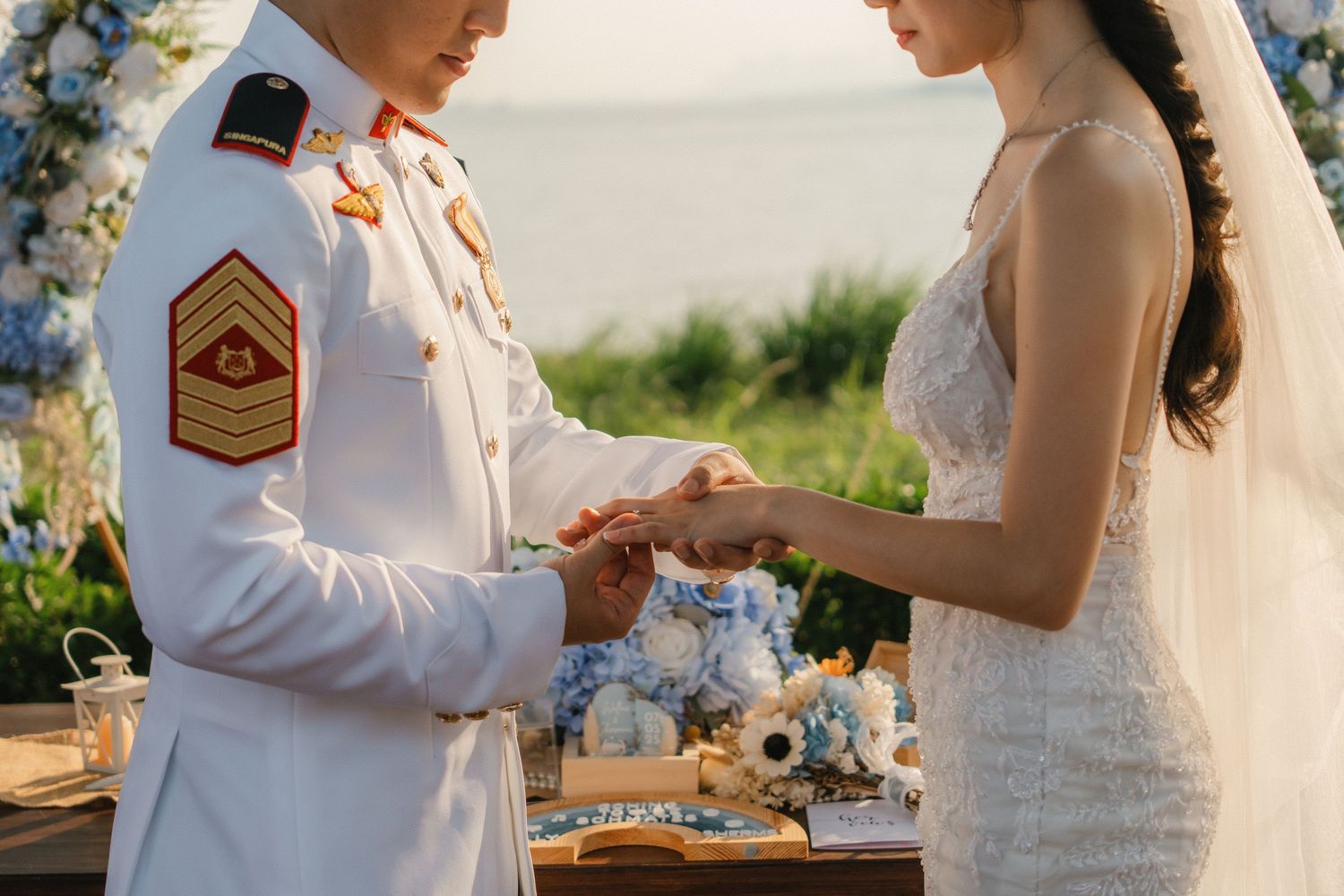 Military service member and bride exchange rings during outdoor summer wedding ceremony.