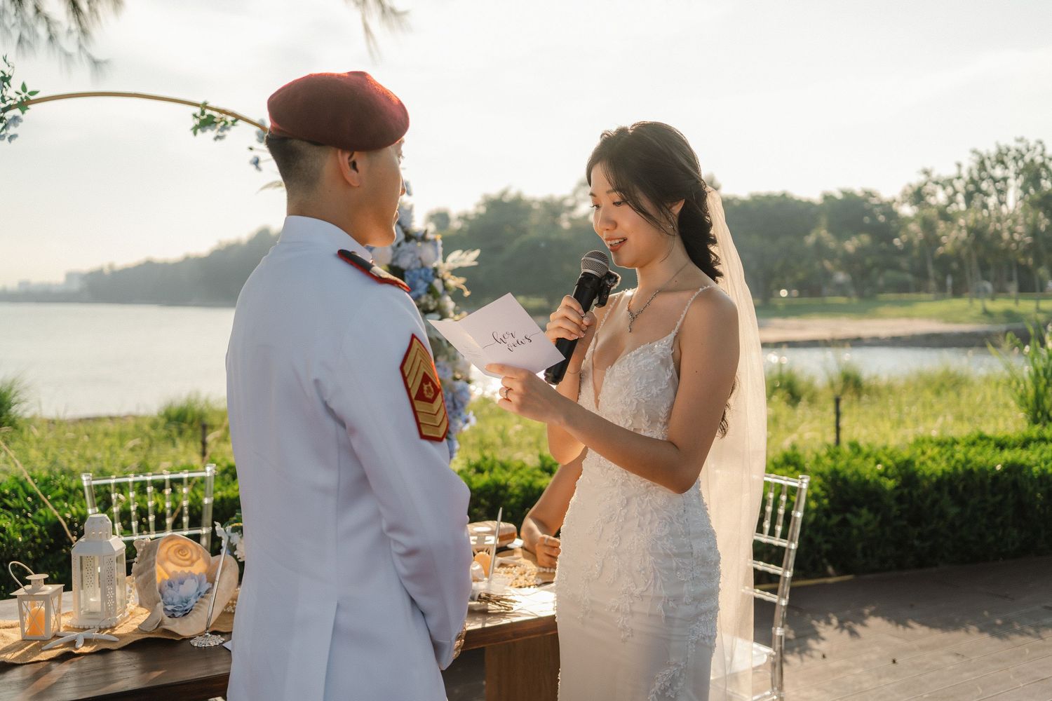 Wedding ceremony setup with white chairs and floral arrangements overlooking waterfront at sunset.