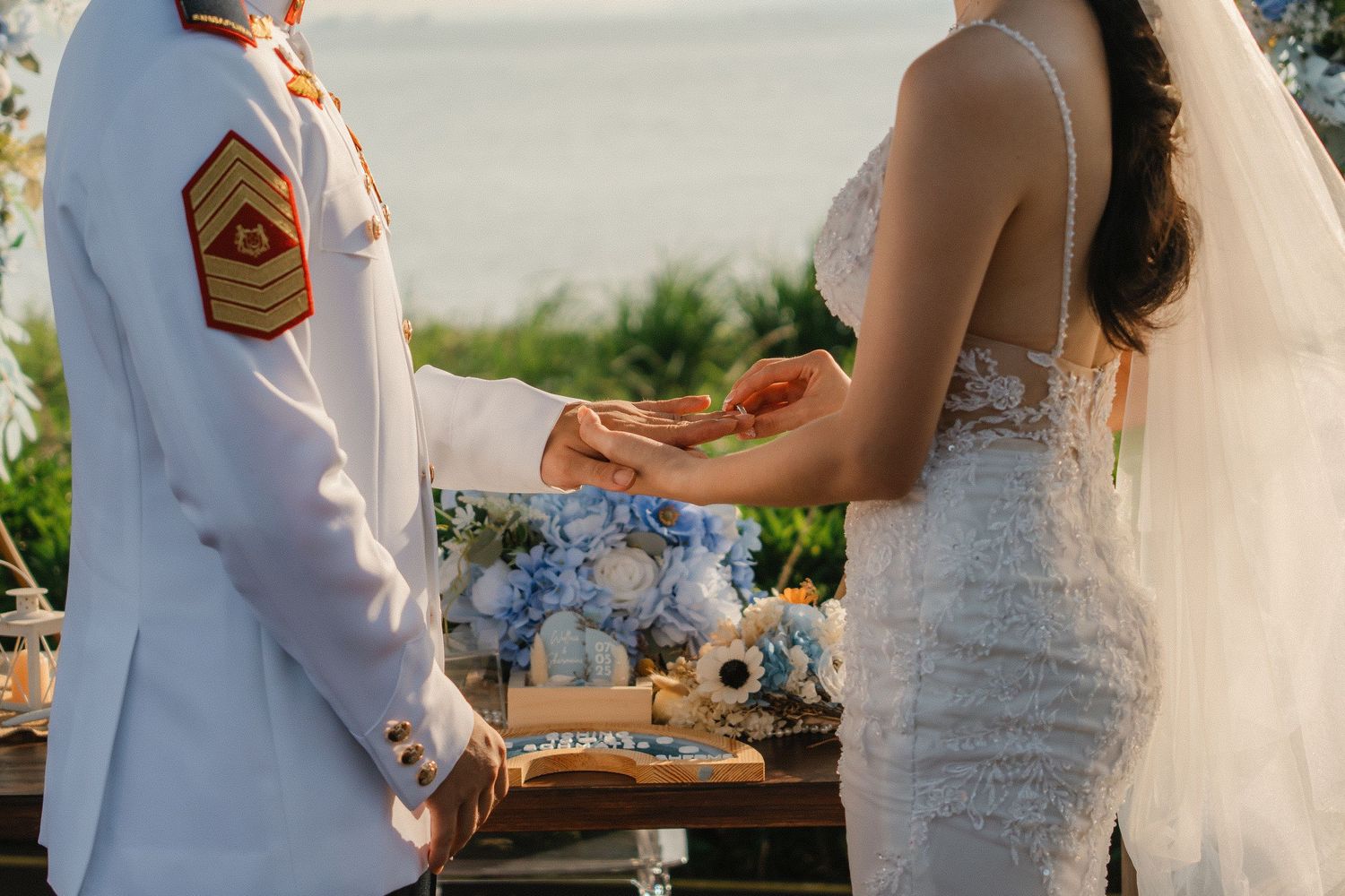 Close up of wedding ceremony with white military uniform and lace dress against ocean backdrop.