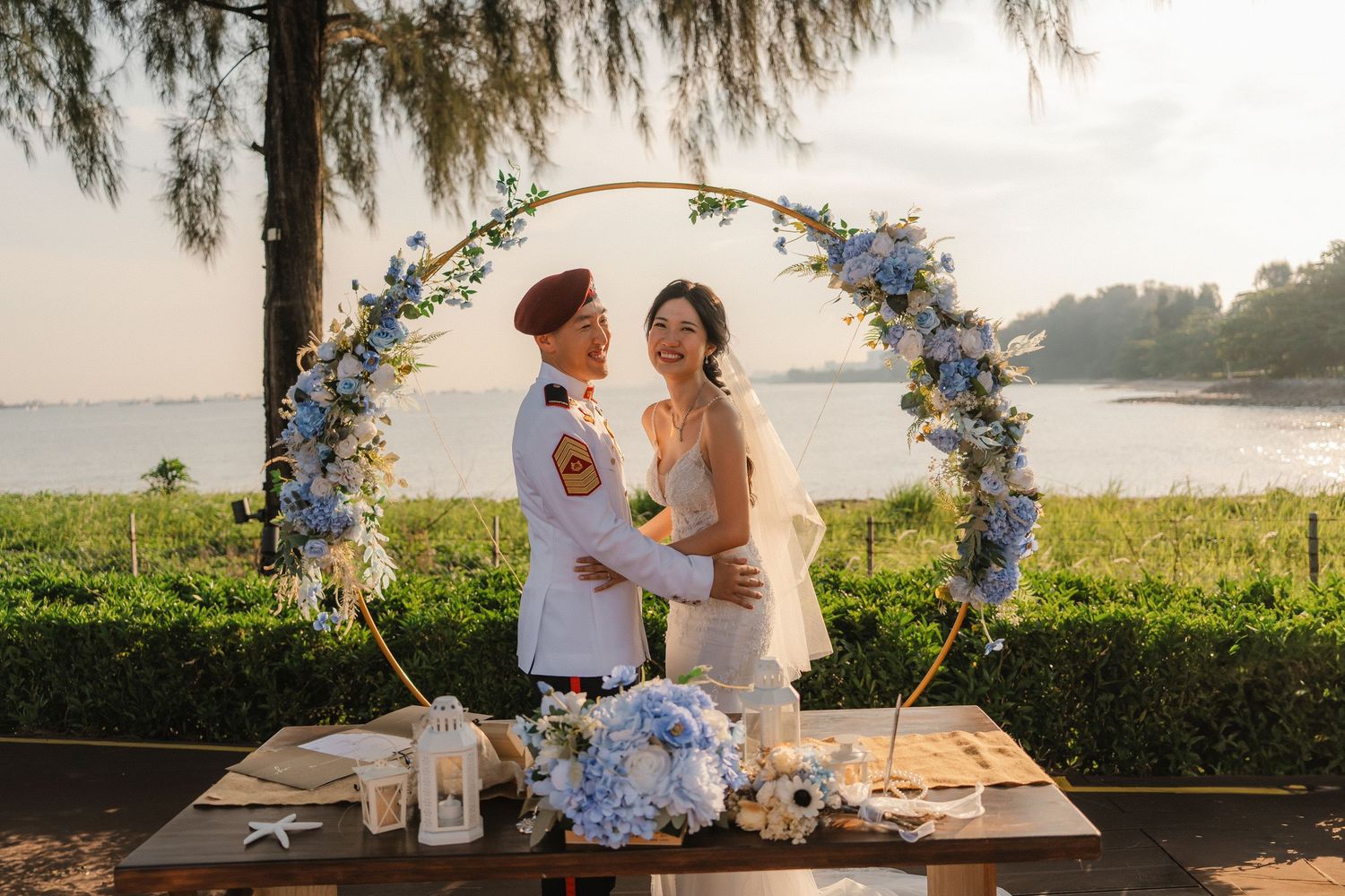 Intimate outdoor wedding ceremony setting with blue floral arch and waterfront views.