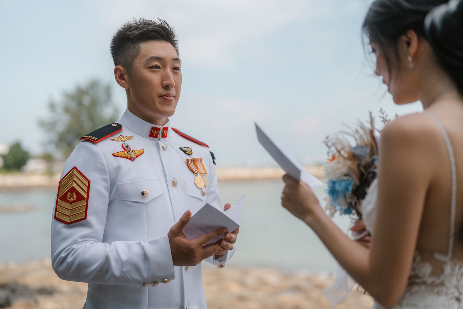 A couple reads personal vows during an intimate outdoor wedding ceremony on a sunny day.