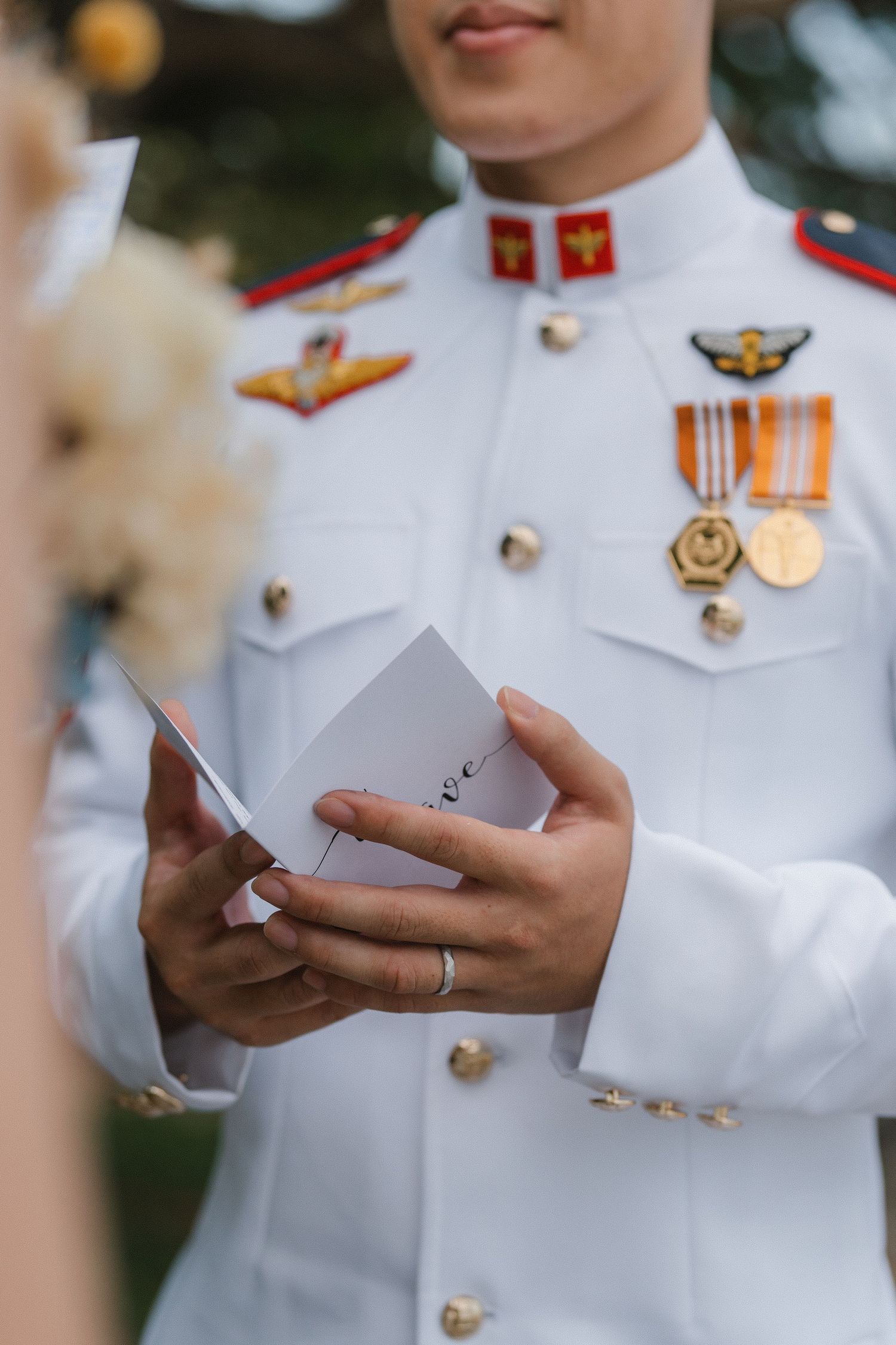 A row of military personnel in white dress uniforms holding small papers or cards during a formal ceremony.