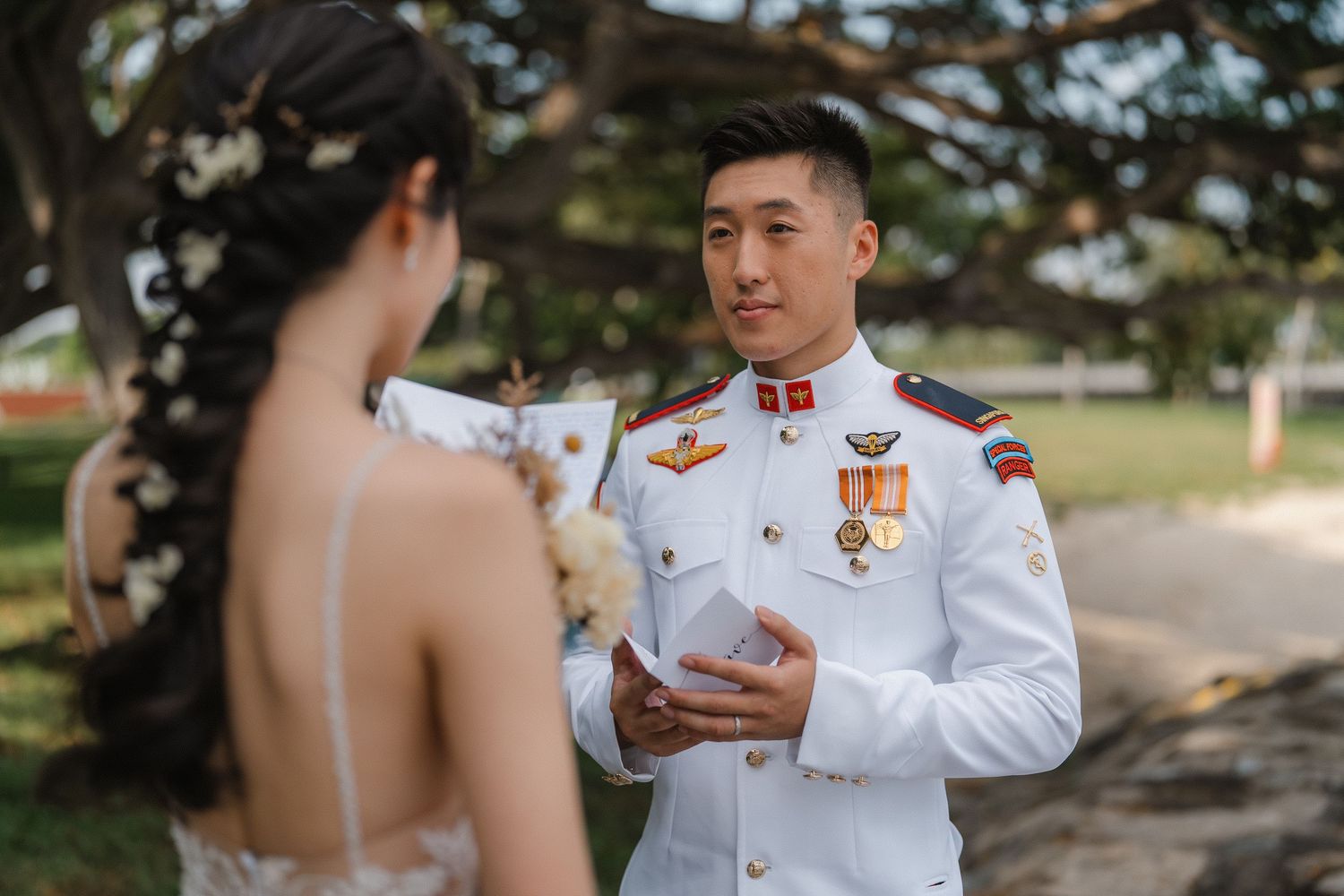 A military groom in decorated white uniform speaks during outdoor wedding photography session.